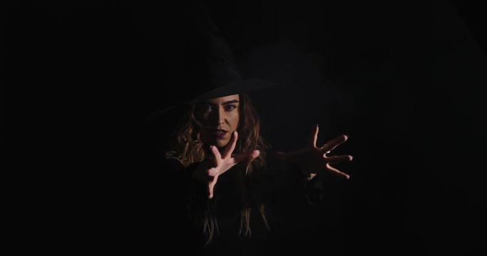 Charming halloween witch recites spells, miracles with smoke over black background. Witchcraft and magic, space for text