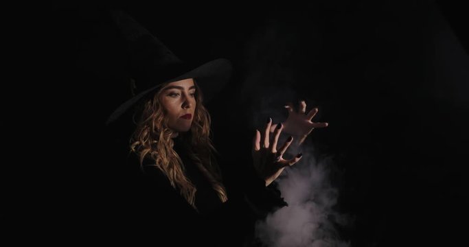 Charming halloween witch recites spells, miracles with smoke over black background. Witchcraft and magic, space for text