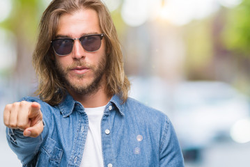 Young handsome man with long hair over isolated background sending message using smartphone pointing with finger to the camera and to you, hand sign, positive and confident gesture from the front