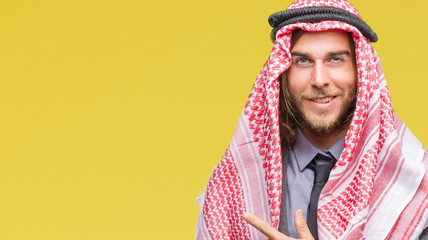 Young handsome arabian man with long hair wearing keffiyeh over isolated background cheerful with a smile of face pointing with hand and finger up to the side with happy and natural expression on face