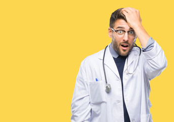 Young handsome doctor man over isolated background surprised with hand on head for mistake,...
