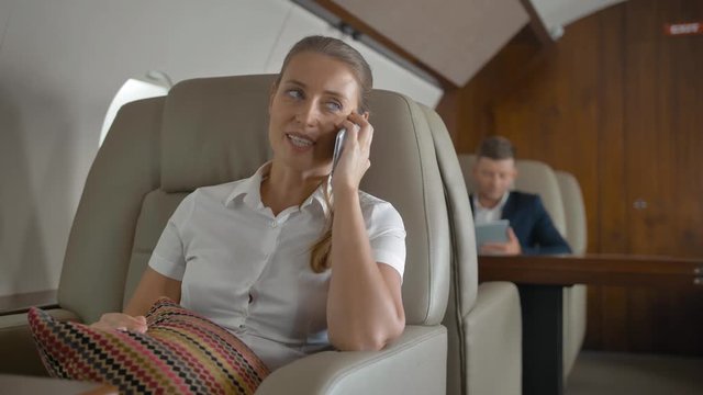 Attractive businesswoman smiling while talking by selphone with her friend in business jet. She happy of comfortable and luxury flight of private aircraft.