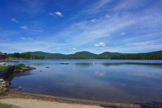 Adirondack Park, New York, USA: View of Blue Mountain in the distance from the shore of Blue Mountain Lake, with while clouds in a deep blue sky above.