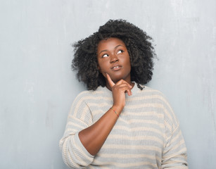 Fototapeta na wymiar Young african american plus size woman over grey grunge wall wearing a sweater with hand on chin thinking about question, pensive expression. Smiling with thoughtful face. Doubt concept.