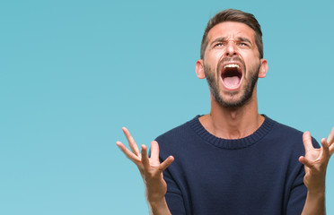 Young handsome man wearing winter sweater over isolated background crazy and mad shouting and yelling with aggressive expression and arms raised. Frustration concept.