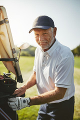 Smiling senior man looking through his golf club bag