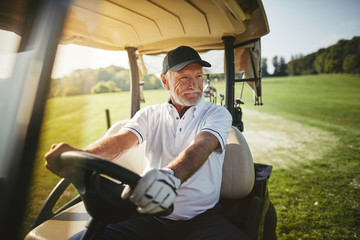 Senior man driving his golf cart on a fairway - obrazy, fototapety, plakaty