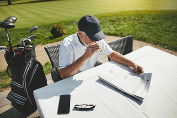 Senior man sitting with coffee at his golf club restaurant