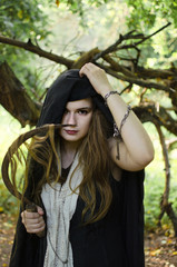 young woman, perhaps a witch in black clothes and a white shawl with a sharp sickle in her hands cut off her hair in order to induce damage and conjure