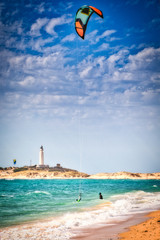 Surfers on the beach of Los Canos de Meca, with the Trafalgar lighthouse in the background, in...