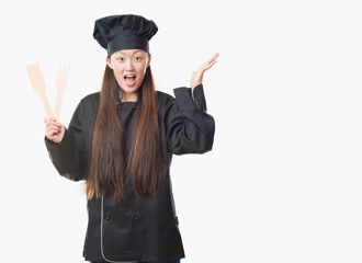 Young Chinese woman over isolated background wearing chef uniform very happy and excited, winner expression celebrating victory screaming with big smile and raised hands