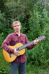 blue-eyed blond in a plaid shirt playing the guitar