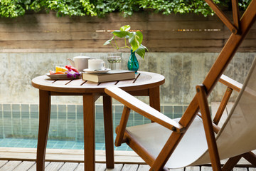 Cup of coffee on top of reading book with fresh fruit on wooden table.