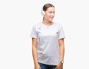 Young caucasian woman listening to music wearing headphones over isolated background looking away to side with smile on face, natural expression. Laughing confident.