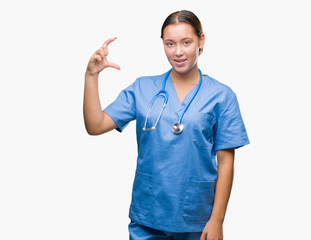 Young caucasian doctor woman wearing medical uniform over isolated background smiling and confident gesturing with hand doing size sign with fingers while looking and the camera. Measure concept.