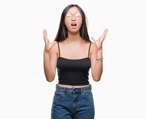 Obraz na płótnie Canvas Young asian woman wearing glasses over isolated background crazy and mad shouting and yelling with aggressive expression and arms raised. Frustration concept.