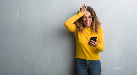 Middle age hispanic woman using smartphone stressed with hand on head, shocked with shame and...