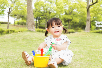 青空をバックに芝生の公園で1人遊ぶ幼い女の子。幸せ、育児、成長、健康、イメージ 