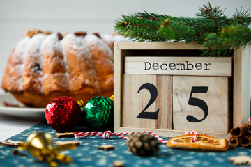 Traditional fruitcake for Christmas decorated with powdered sugar and nuts, raisins next to wooden calendar with date 25 december Delicioius Homemade Pastry. New year and Christmas celebration concept - obrazy, fototapety, plakaty