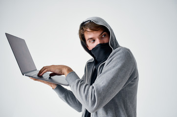 man holding a laptop on his hand in a hood in a dark mask