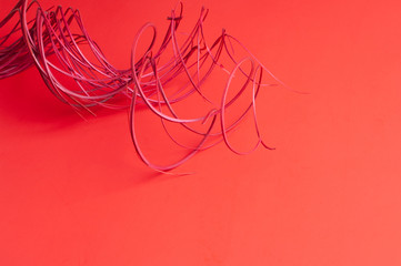 A bunch of  wavy and swirly red painted wooden sticks serve as a focal point on a subtly gradient and lightly textured red paper background.