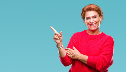 Atrractive senior caucasian redhead woman wearing winter sweater over isolated background with a big smile on face, pointing with hand and finger to the side looking at the camera.