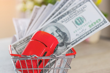 Red car and pile of one hundred dollar bills in basket on table. Earn money for a better life. Business, financial and banking concept or ideas for saving money.