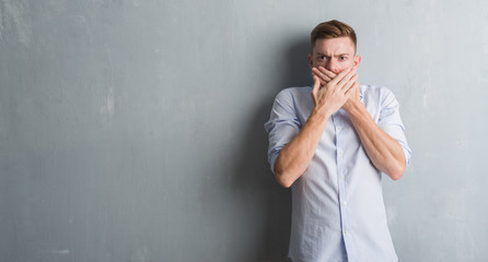 Young redhead business man over grey grunge wall shocked covering mouth with hands for mistake. Secret concept.