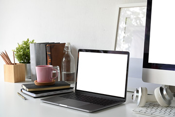 Blank screen laptop with blank poster and office supplies.