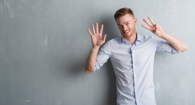 Young redhead business man over grey grunge wall showing and pointing up with fingers number eight while smiling confident and happy.