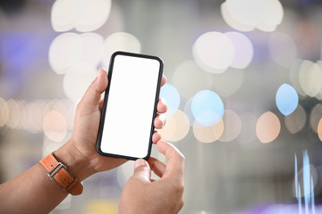 Male hand holding blank screen mobile phone over night street bokeh.