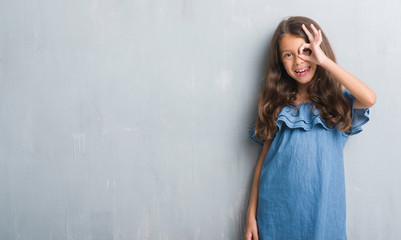 Fototapeta premium Young hispanic kid over grunge grey wall doing ok gesture with hand smiling, eye looking through fingers with happy face.