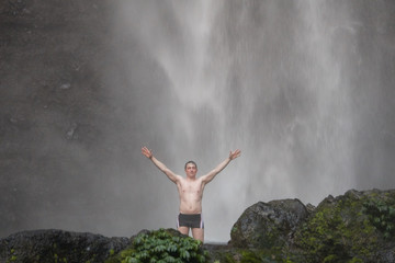 Fototapeta na wymiar A happy man standing uder Sekumpul waterfall in Bali, Indonesia