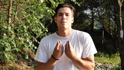 Young handsome man standing in nature, doing typical Italian gesture meaning a general question