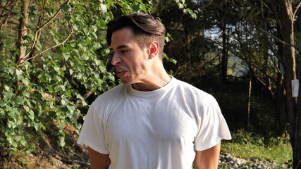Young rude handsome man standing in nature, spitting on the ground