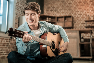 Favourite music. Joyful happy good looking man holing the guitar and smiling while playing music