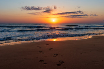 Fototapeta na wymiar Amazing colorful sunrise at sea, footprints in the sand