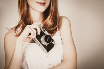young redhead girl in a white dress holding a classic camera on a white background