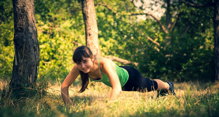 Naklejka na ściany i meble Young beautiful girl doing physical exercises in a park. Summer season