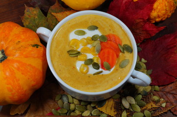Spicy pumpkin soup in a white bowl on a background of colorful pumpkins. selective focus
