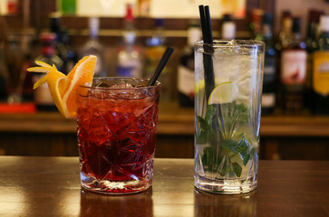 Drinks concept. Cold transparent cocktails with ice cubes. Blur bottles background, close up view.