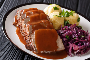 Delicious traditional German dinner Sauerbraten - slowly stewed marinated beef with gravy with potato dumplings and red cabbage close-up. horizontal © FomaA