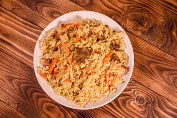 Ceramic plate with pilaf on wooden table. Top view