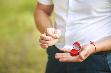 A man makes a proposal to his beloved. Male hand holds wedding ring on the background of green nature.