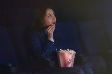 Naklejka premium Young woman watching movie and eating popcorn in cinema