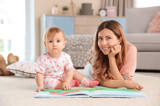 Young mother with baby reading book on carpet at home