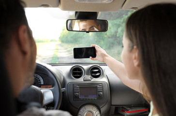 Young couple taking selfie in car on road trip. Back view - Powered by Adobe