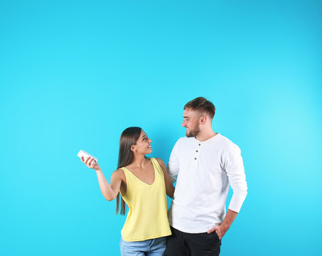 Young couple with air conditioner remote on color background