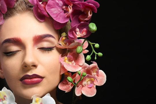 Young woman with dyed eyebrows surrounded by flowers on black background