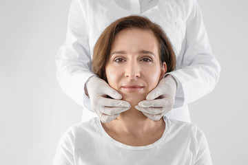Doctor examining mature woman face before cosmetic surgery on white background